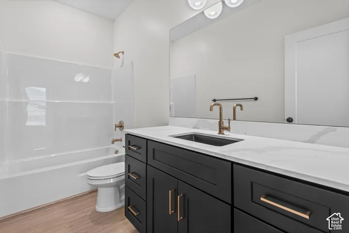 Wood-finish flooring, white tub and shower surround, black vanity with white countertop, gold-toned faucet, and rectangular undermount sink