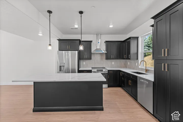 Kitchen featuring an island with a light-toned countertop, dark cabinetry with gold-toned hardware, stainless steel appliances, and wood-finish flooring