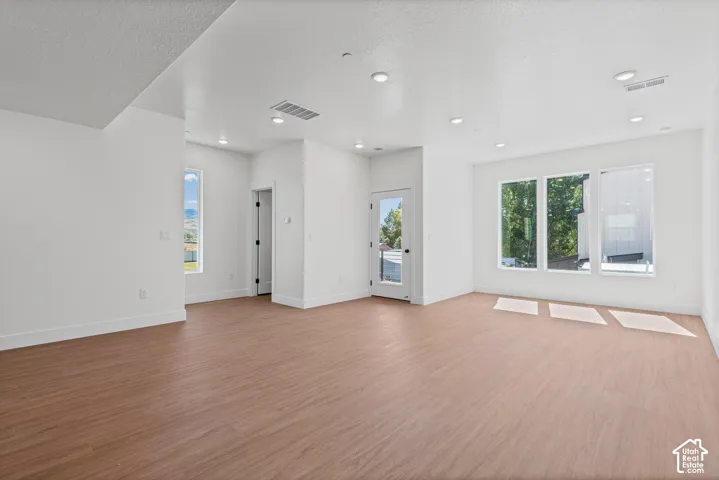 Spacious interior with wood-finish flooring, recessed lighting, multiple windows, and a glass-paneled door