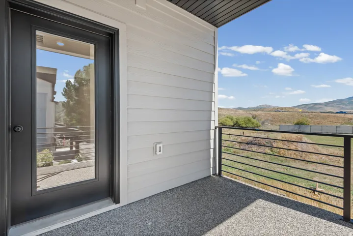 Private balcony featuring a textured floor, black frame glass panel door, and metal railing