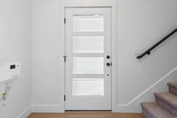 White interior door with four frosted glass panels and matte black hardware, accompanied by a black wall-mounted handrail and a carpeted staircase