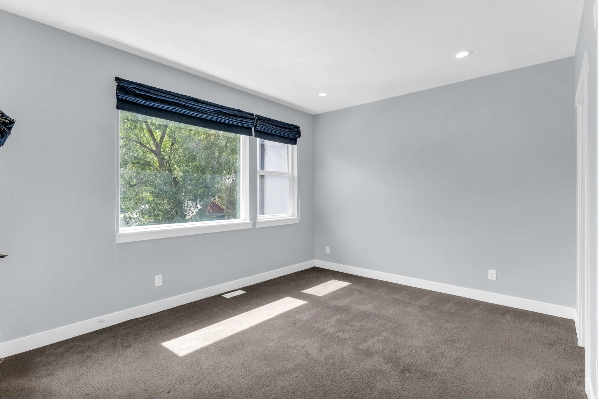 Spacious room with light gray walls, dark carpet flooring, and white trim