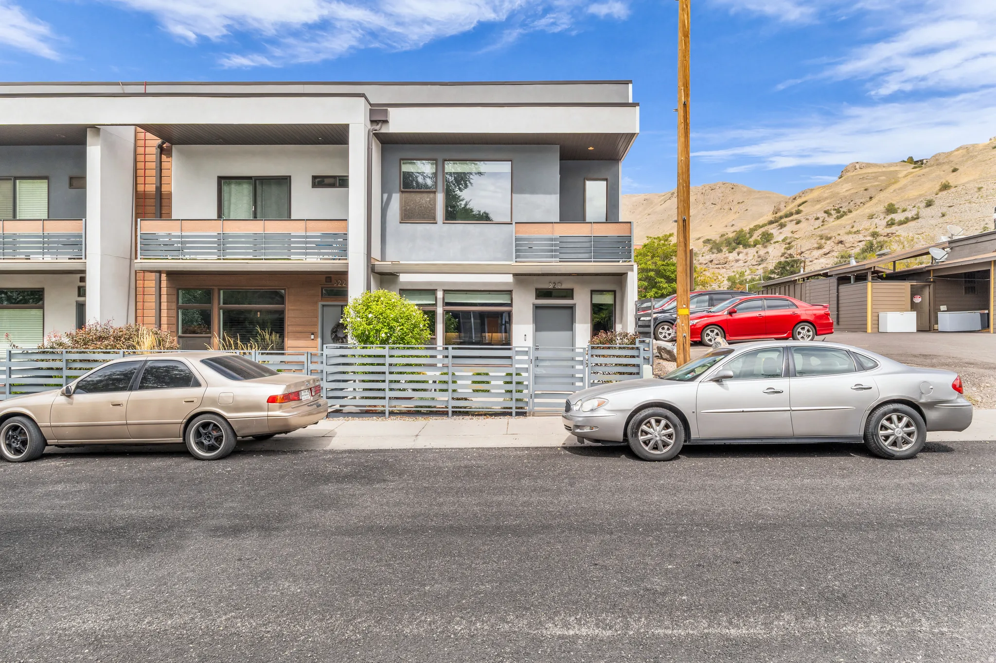 Modern exterior with flat roofline, stucco and wood-finish siding, multiple balconies with metal railings, and a fenced front entry