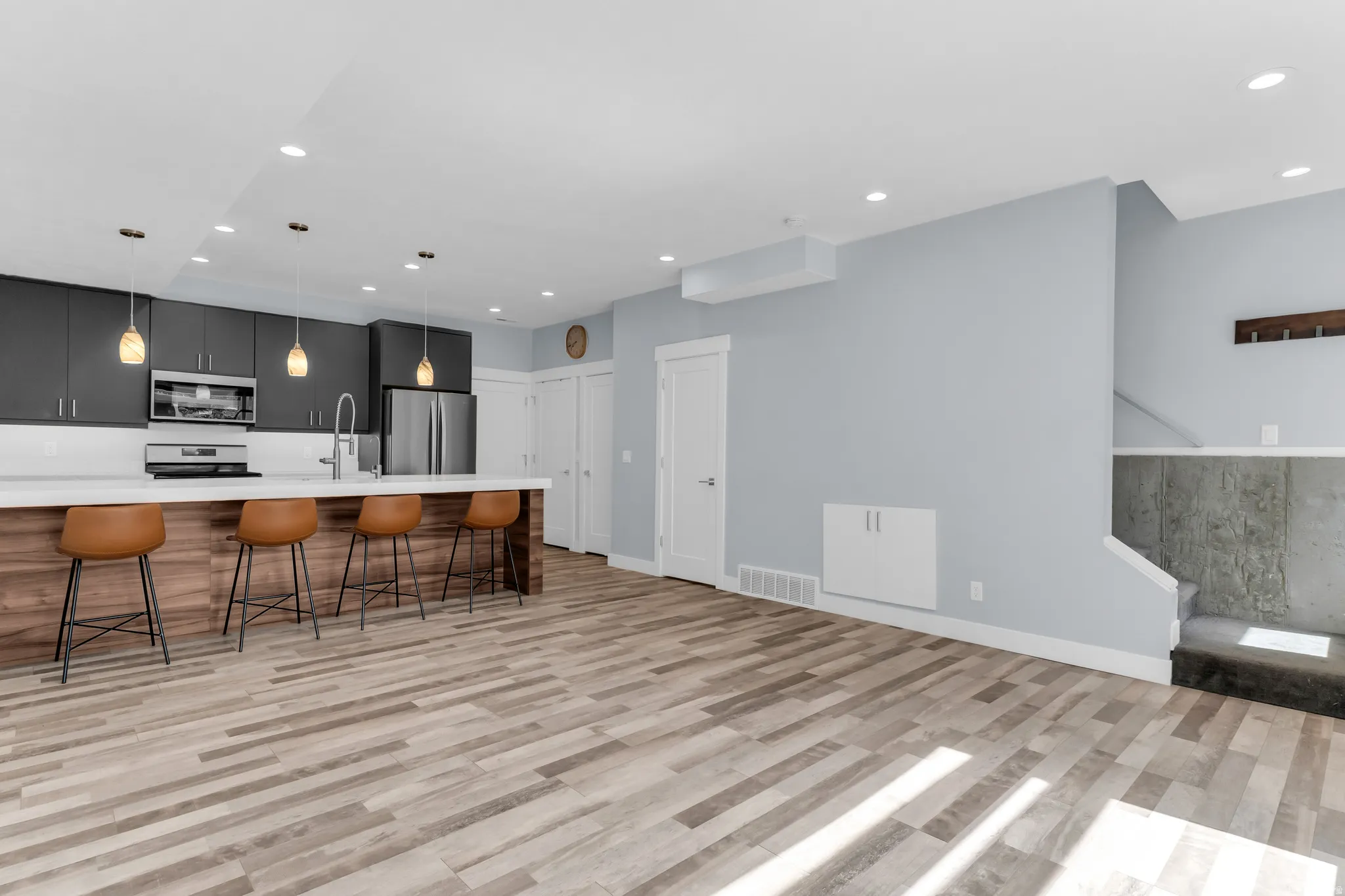 Open-concept living area with wood-finish flooring, recessed lighting, and a modern kitchen featuring dark cabinetry and a white countertop