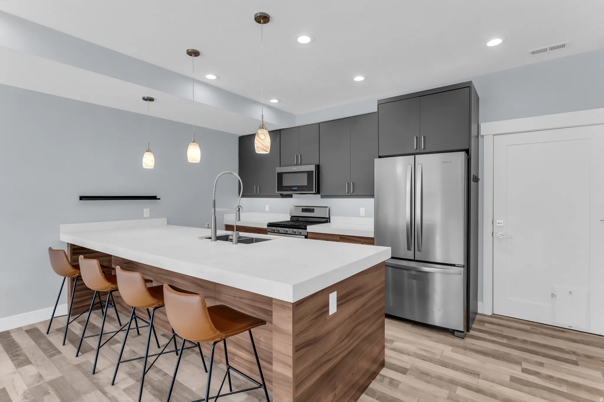 Kitchen featuring wood-finish flooring, dark gray cabinetry, stainless steel appliances, a center island with a white countertop, and pendant lighting