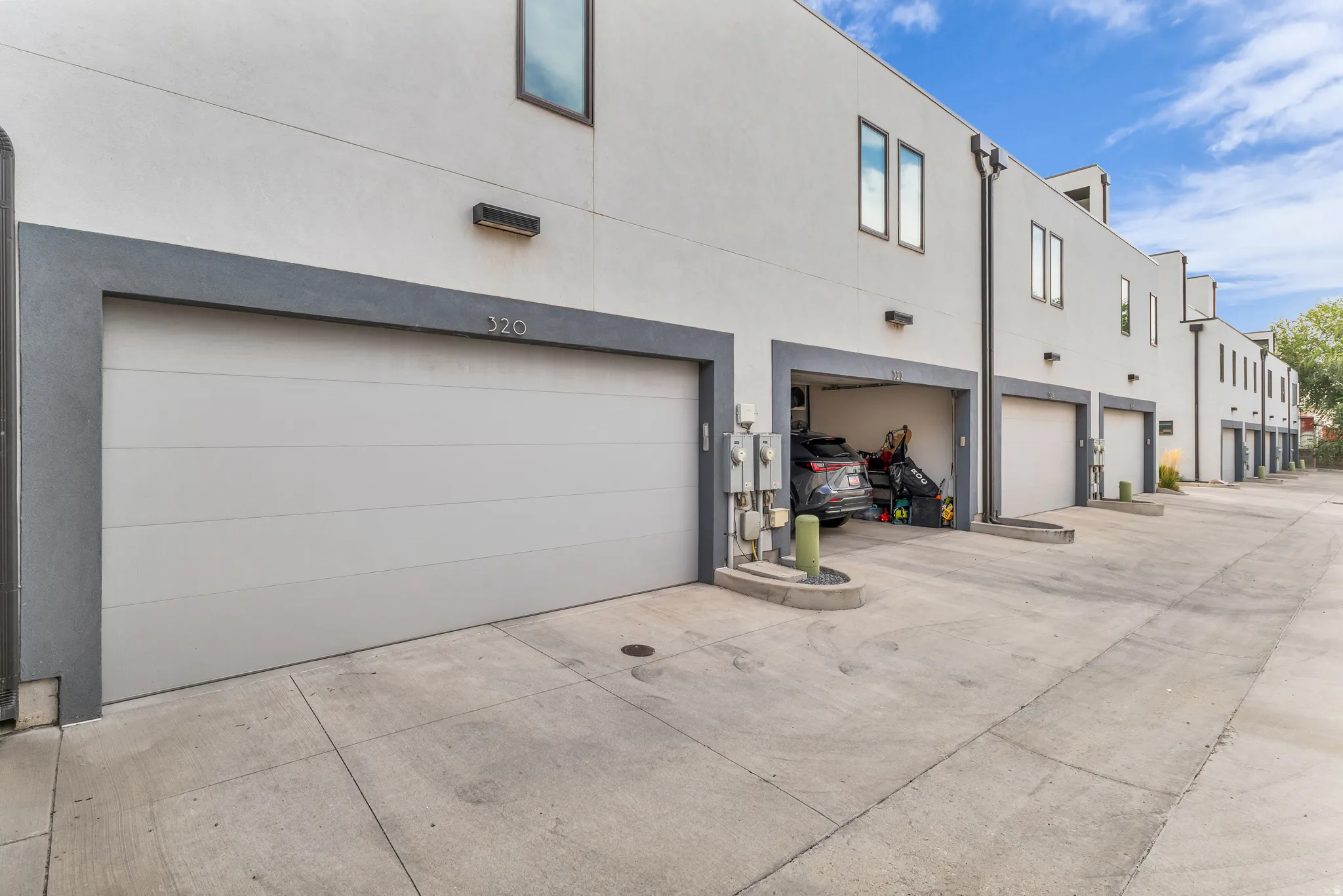 Attached garage with a panel door, concrete drive, exterior lighting, and stucco facade