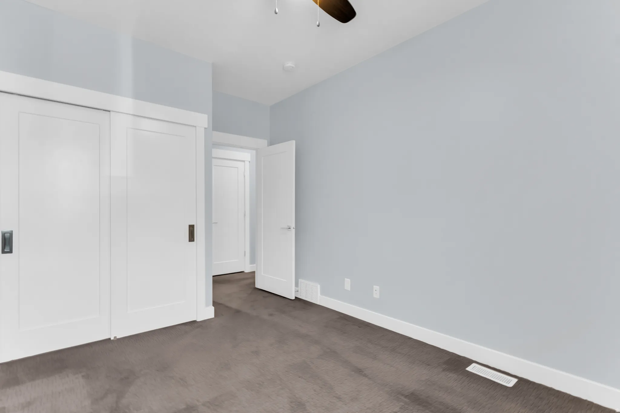 Sliding panel closet doors with dark hardware, light gray wall finish, white trim, and a dark carpeted floor