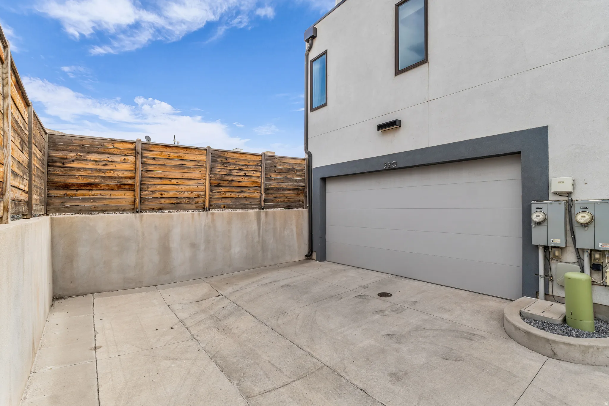 Concrete driveway with a modern garage door, wood plank fencing, and stucco exterior