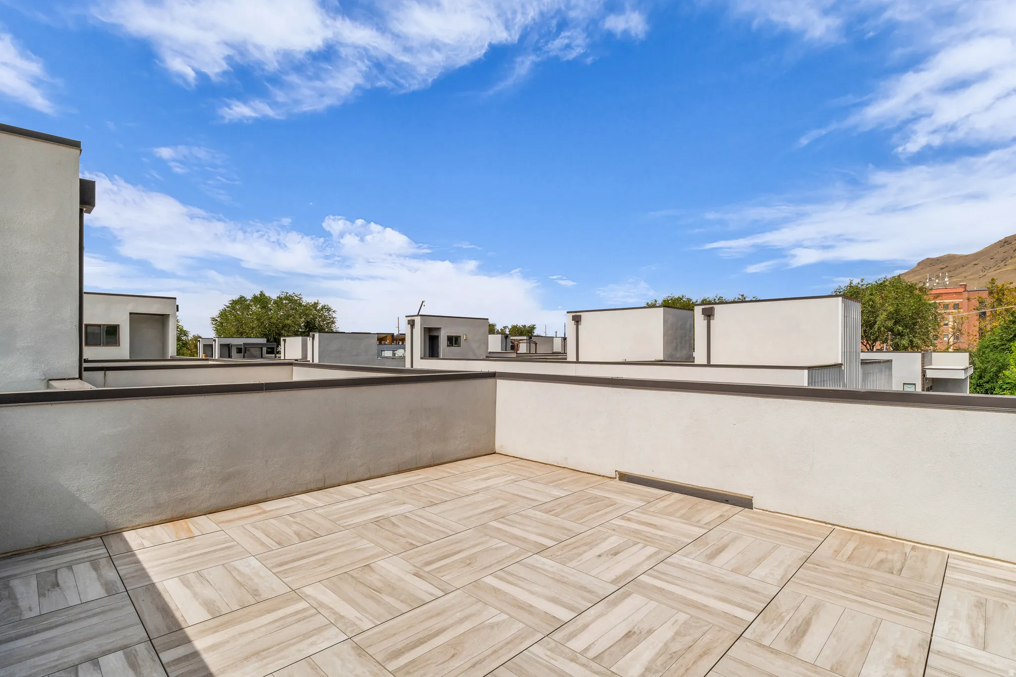 Rooftop patio featuring light-toned tile flooring and stucco walls with dark coping