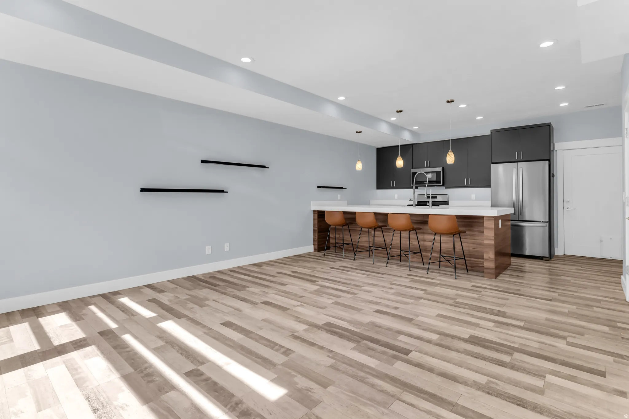 Open-concept kitchen featuring dark wood-finish cabinetry, stainless steel appliances, a white countertop island, and pendant lighting