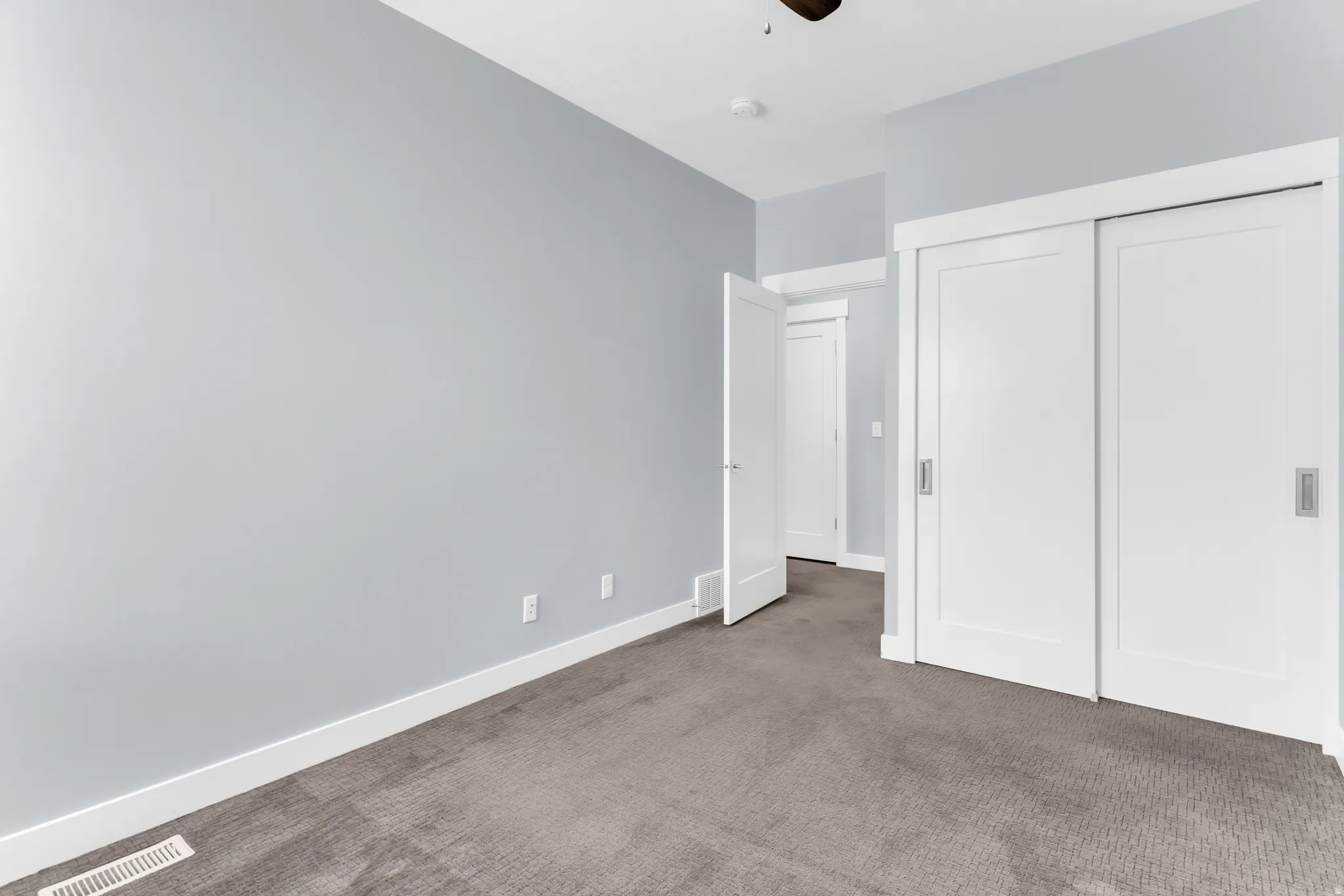 Plush grey carpeting, light blue wall finishes, white trim, and sliding white doors with recessed pulls