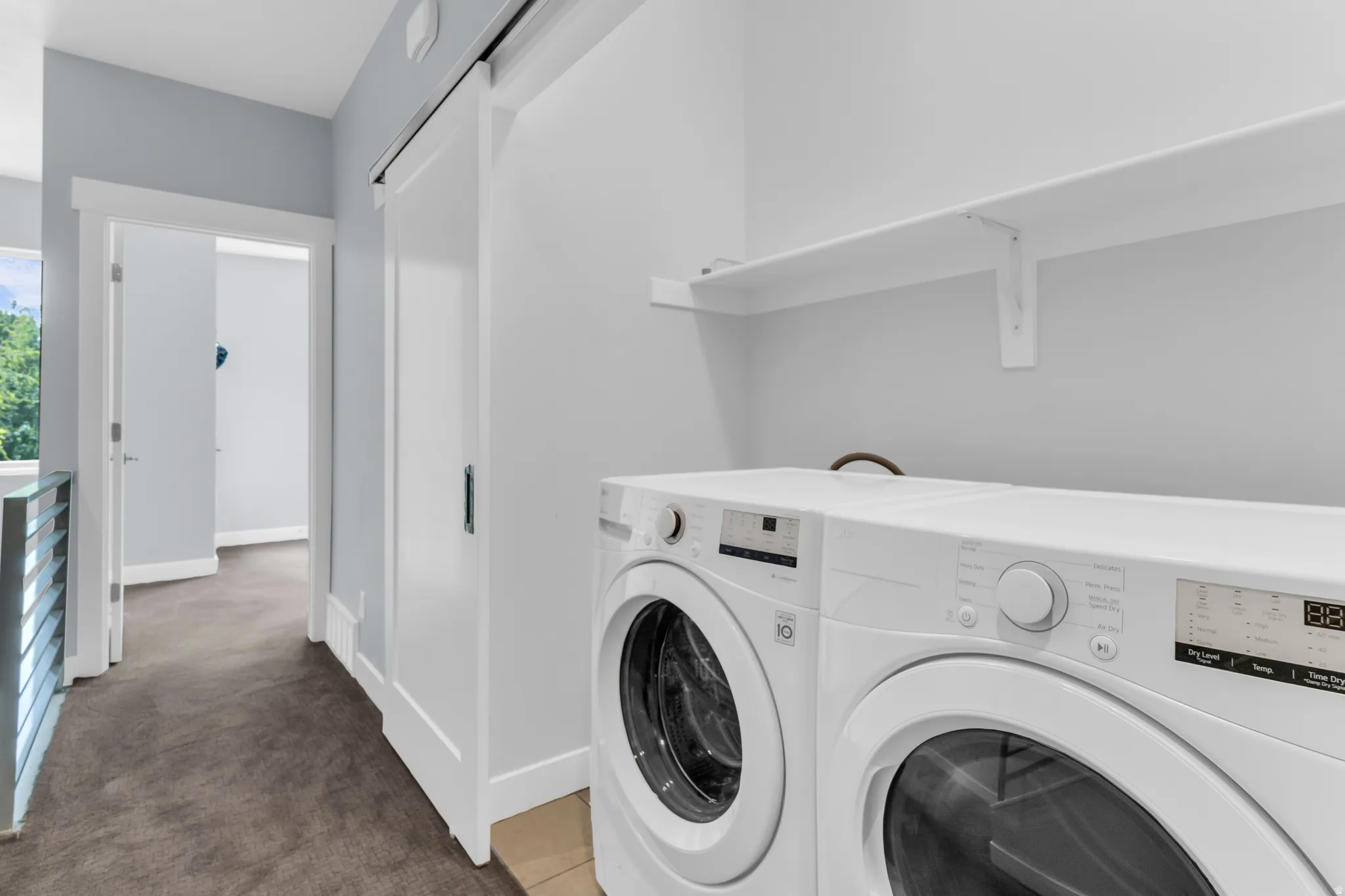 Built-in laundry appliances, overhead shelving, white barn door, and corridor access