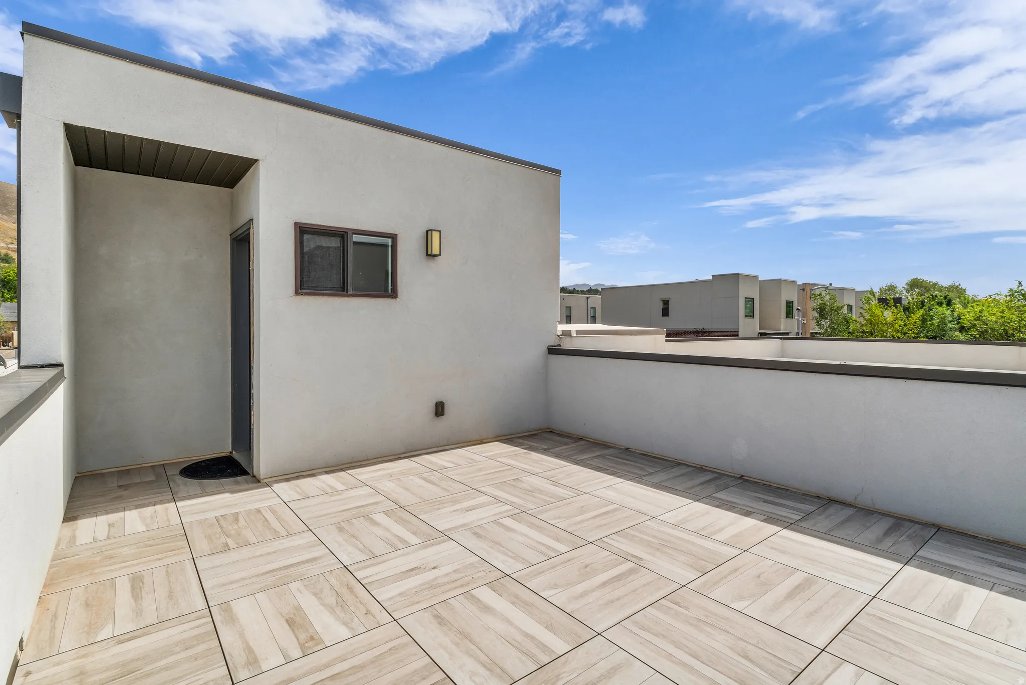 Rooftop deck featuring light-toned tile flooring, stucco exterior walls, and a contemporary wall-mounted light fixture
