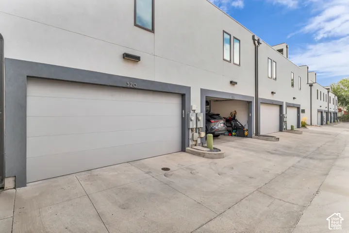 Attached garage with a panel door, concrete drive, exterior lighting, and stucco facade
