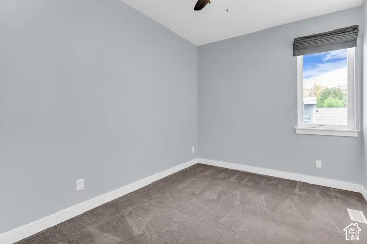 Light gray walls with white trim, gray carpet, single window with a privacy shade, and a ceiling fan