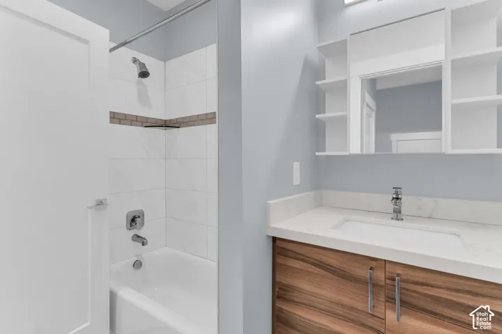 Bathroom featuring a white bathtub with a tiled shower surround, a wood-finish vanity with an integrated sink, a light-colored countertop, and a mirrored medicine cabinet with open shelving