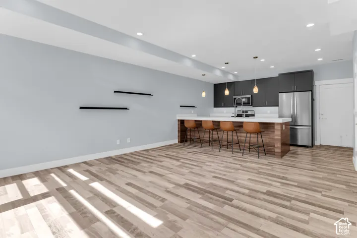 Open-concept kitchen featuring dark wood-finish cabinetry, stainless steel appliances, a white countertop island, and pendant lighting