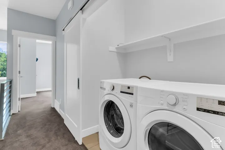 Built-in laundry appliances, overhead shelving, white barn door, and corridor access