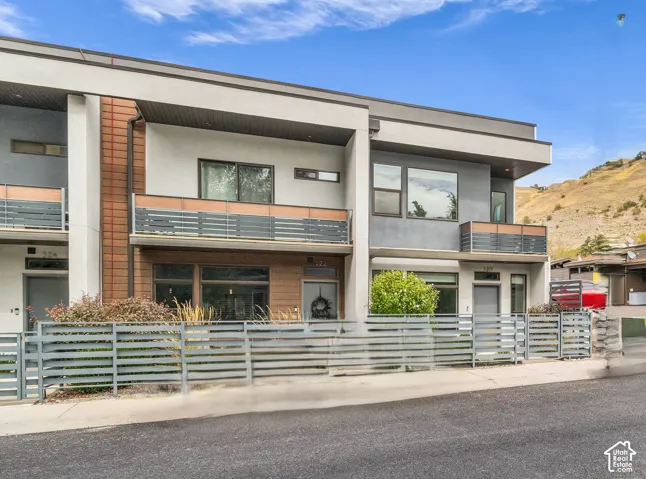 Modern architectural exterior featuring multiple balconies, a horizontal slat fence, a contrasting multi-textured facade, and a flat roofline