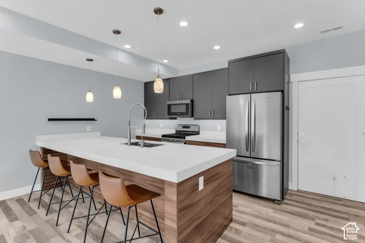 Kitchen featuring wood-finish flooring, dark gray cabinetry, stainless steel appliances, a center island with a white countertop, and pendant lighting