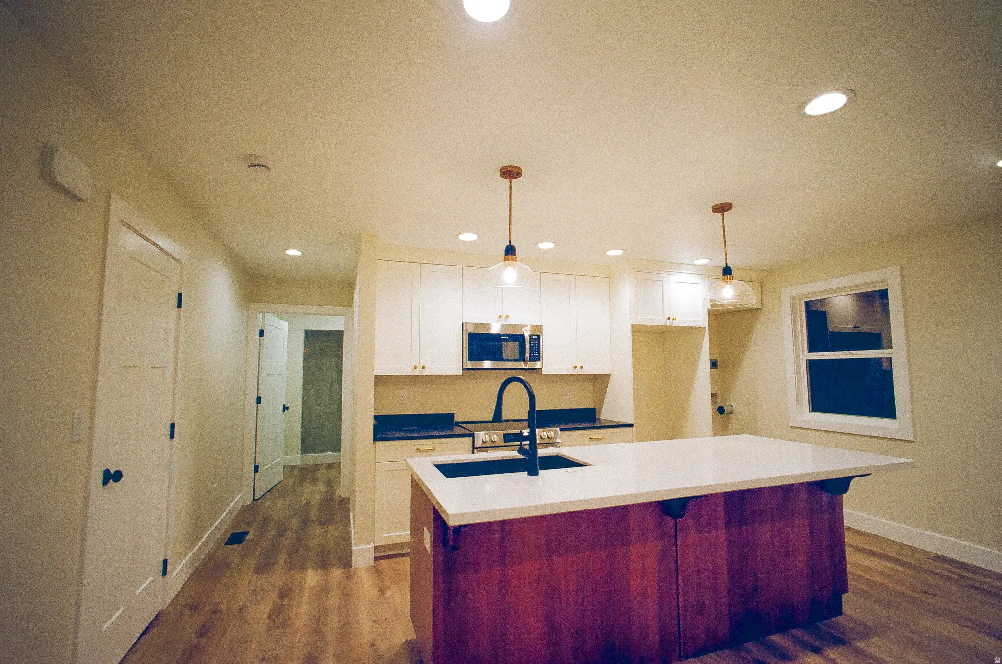 Kitchen featuring an island with a built-in sink, white cabinetry with gold-tone hardware, wood-finish flooring, and recessed lighting