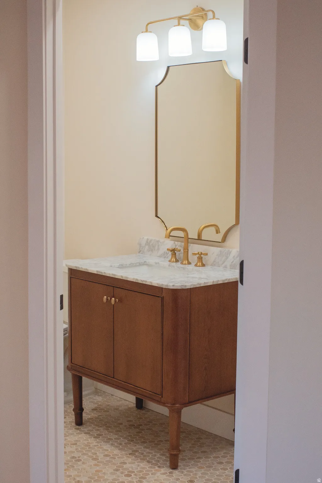 Wood-finish vanity with a stone countertop, undermount sink, and brass-tone fixtures