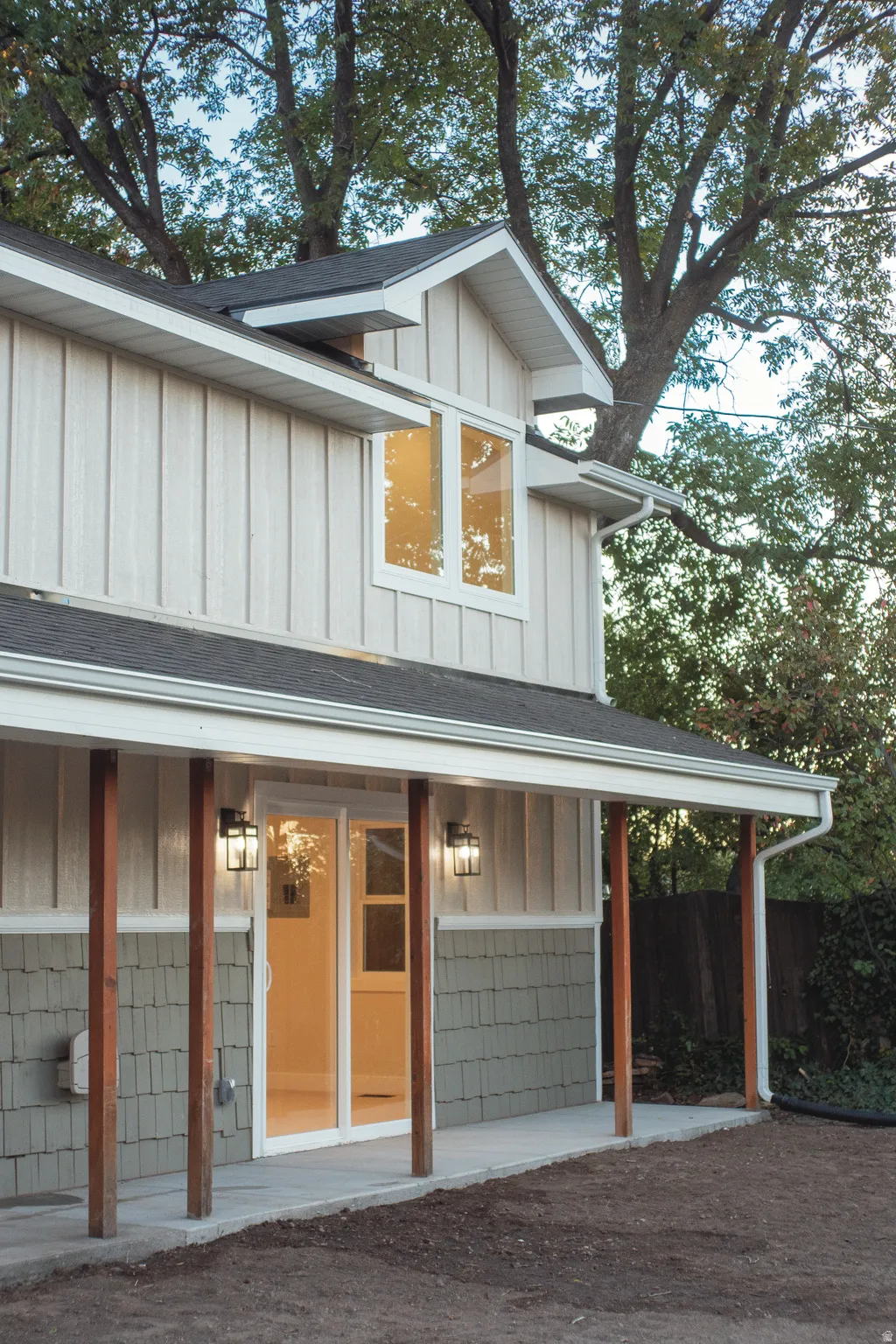 Board and batten siding, shake siding, covered patio with wood columns, sliding glass door, and exterior lighting fixtures