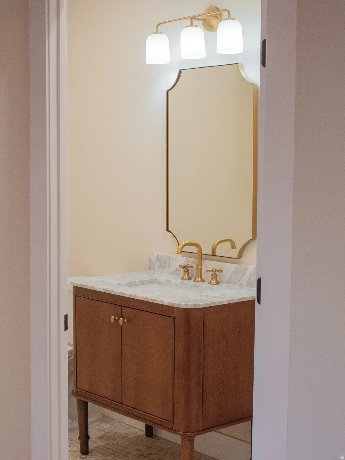 Wood-finish vanity with a stone countertop, undermount sink, and brass-finish faucet