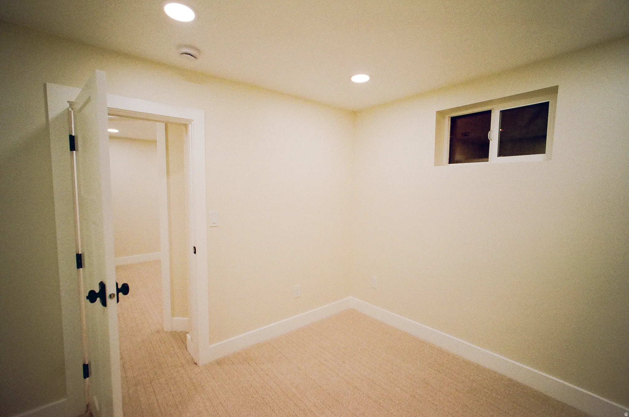 Recessed lighting, light-toned carpeting, white trim, and a window for natural light