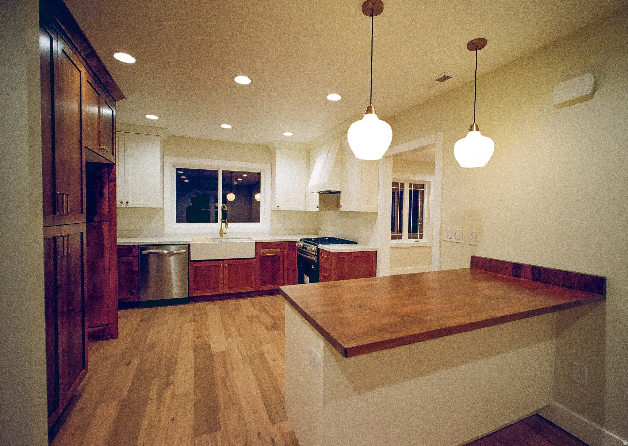 Kitchen featuring wood-finish flooring, two-tone cabinetry, stainless steel appliances, a farmhouse sink, and a wood-finish island countertop