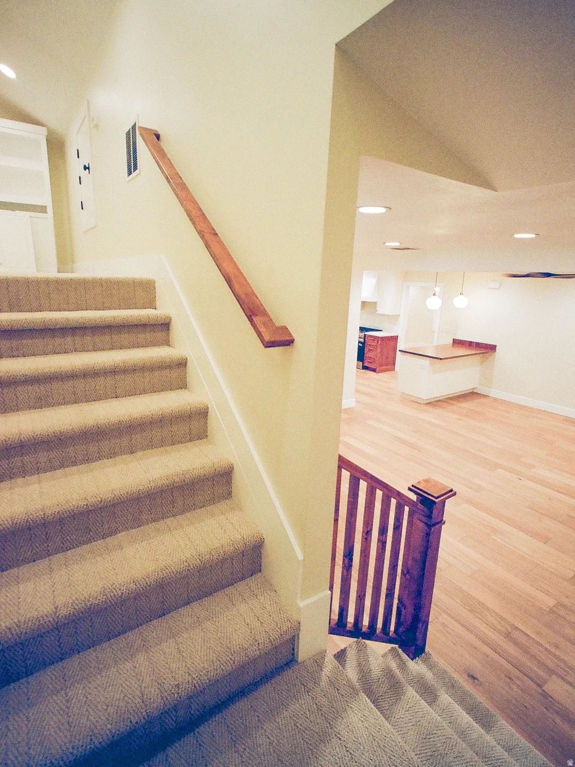 Staircase with wood railing and carpeted treads, leading to a lower level featuring recessed lighting, pendant lighting, and wood-finish flooring