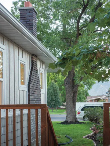 Brick chimney with a terracotta flue cap, white board and batten siding, white framed windows, and a wood railing