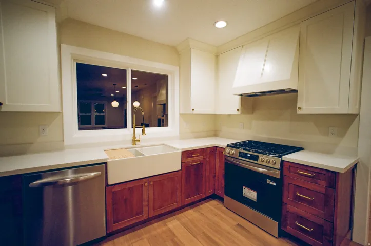 Kitchen featuring a stainless steel range, farmhouse sink, wood-finish flooring, white upper cabinetry, and wood-tone lower cabinetry