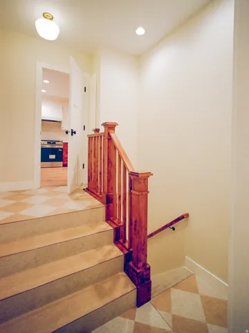 Hardwood newel post and balusters, wood-finish handrail, checkered tile flooring, recessed lighting, and a surface-mounted ceiling fixture