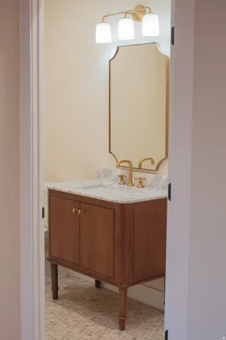 Wood-finish vanity with a stone countertop, undermount sink, and brass-tone fixtures