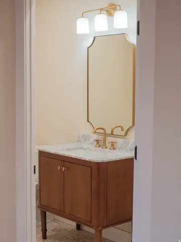 Wood-finish vanity with a stone countertop, undermount sink, and brass-finish faucet