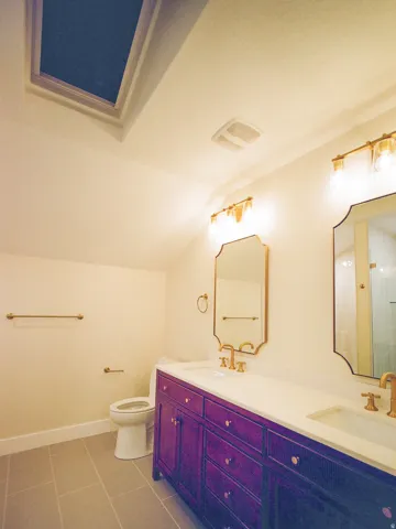 Dual vanity with a white countertop and purple-stained cabinetry, featuring gold-toned fixtures and two framed mirrors