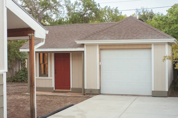 Attached garage with a panel door, concrete driveway, and covered entry with a red door