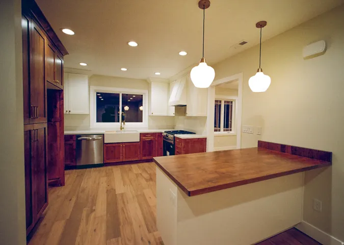 Kitchen featuring wood-finish flooring, two-tone cabinetry, stainless steel appliances, a farmhouse sink, and a wood-finish island countertop