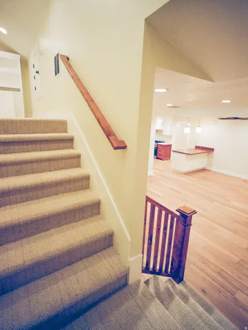 Staircase with wood railing and carpeted treads, leading to a lower level featuring recessed lighting, pendant lighting, and wood-finish flooring