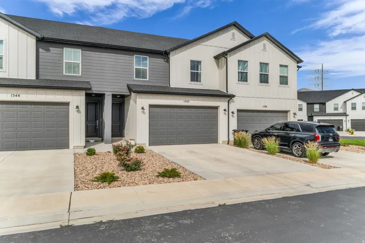 Modern townhome exterior with a dark gray roof, two-car garage, white vertical board siding, and dark gray horizontal siding