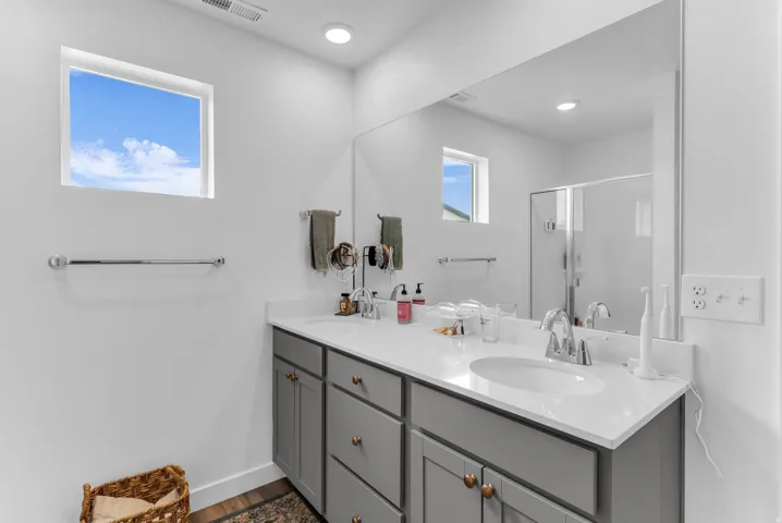 Dual vanity with white countertop and integrated sink, gray cabinetry with brass-tone hardware, and a large wall-mounted mirror
