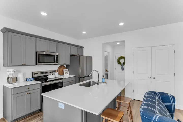 Kitchen with gray shaker-style cabinetry, stainless steel appliances, and a central island featuring an undermount sink and light-toned countertop