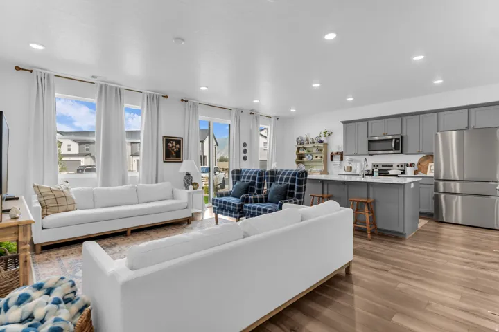 Open-concept living space featuring wood-finish flooring, recessed lighting, a kitchen island with seating, stainless steel appliances, and a sliding glass door