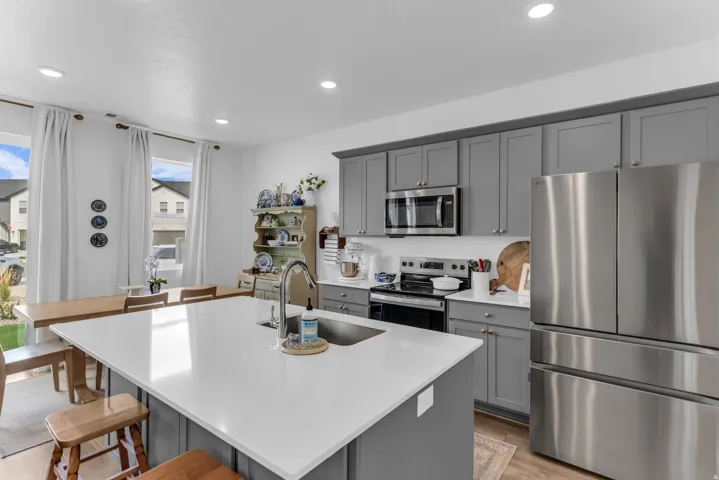 Spacious kitchen featuring gray cabinetry, stainless steel appliances, a center island with sink, ample counter space, and recessed lighting