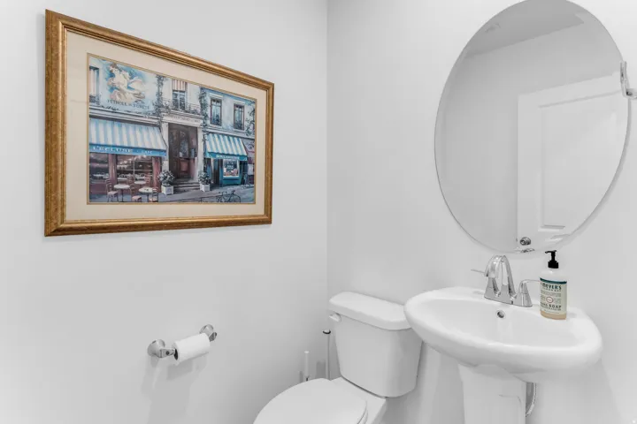 Pedestal sink with chrome faucet, oval mirror, and white toilet