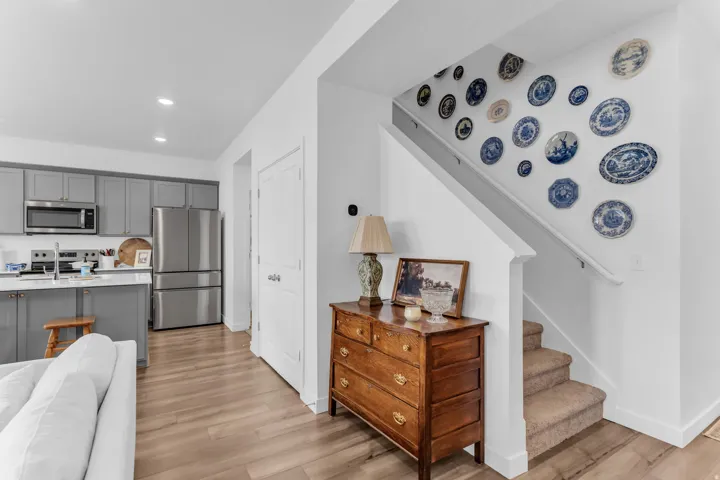 Open-concept living space with wood-finish flooring, recessed lighting, gray cabinetry, stainless steel appliances, and a carpeted staircase