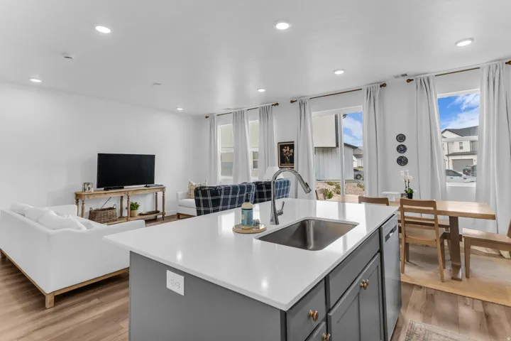 Open-concept living space with recessed lighting, wood-finish flooring, a kitchen island with an undermount sink and a gooseneck faucet, and large windows with white curtains