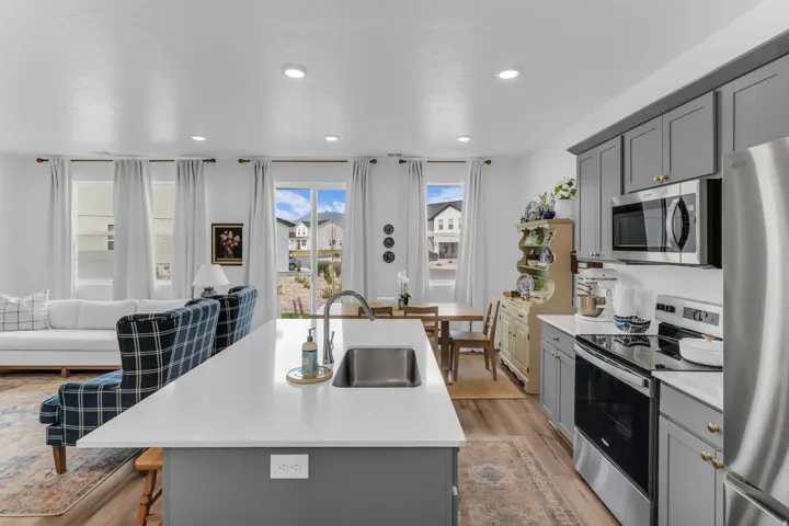 Kitchen island with an undermount sink, stainless steel appliances, grey cabinetry, and wood-finish flooring