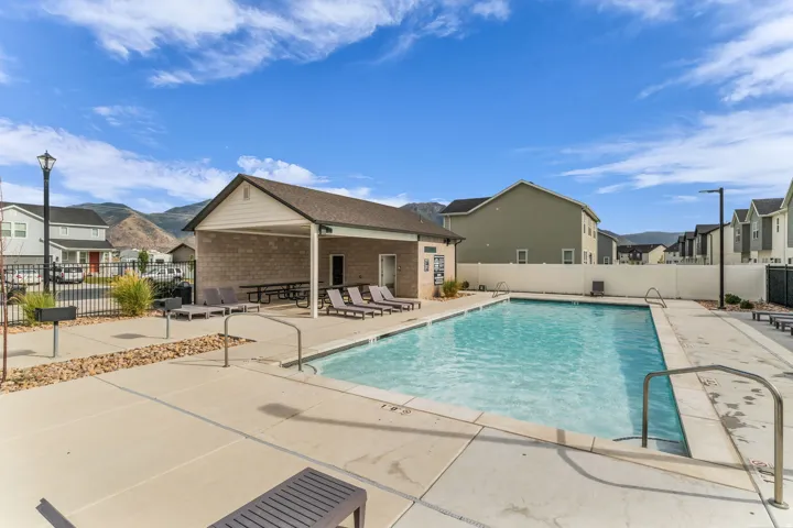 Outdoor swimming pool with concrete decking, covered patio area, mountain backdrop, and surrounding fencing